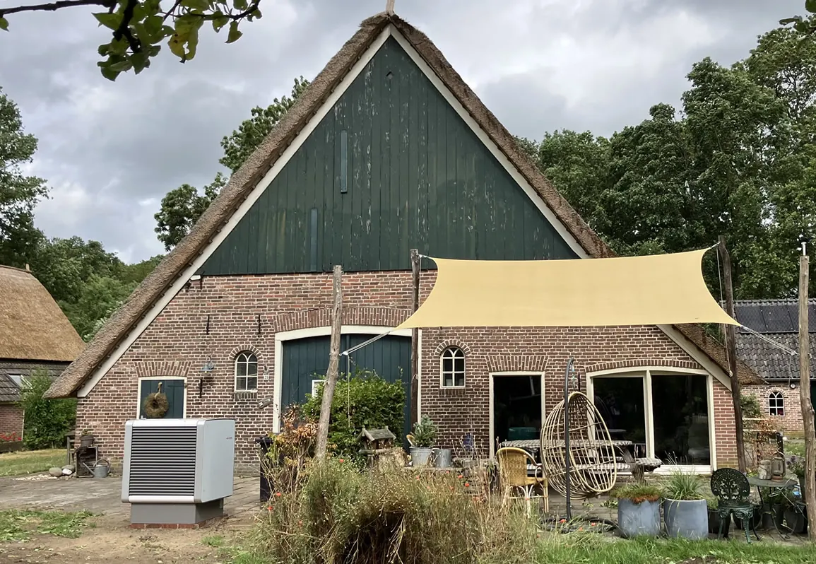 Woonboerderij met rieten dak en een Heliotherm buitenunit naast het huis